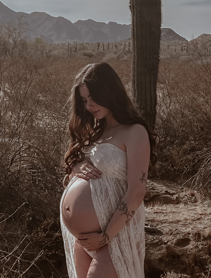 a pregnant woman standing in front of a desert and cacti 